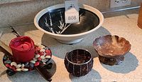 View of the large ceramic bowl with bamboo design, beaded votive candle holder, polished coconut shell dish, and red candle on decorated stand.
