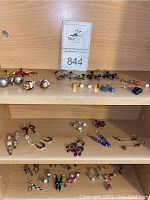 Multiple pairs of assorted earrings displayed on wooden shelves including pearl and beaded varieties