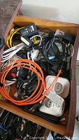 Top view of drawer containing mixed cables in orange, white, black, and yellow, along with power adapters, connectors, and a remote control.