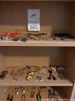 Overview of multiple shelves showcasing a variety of jewelry including orange beaded necklaces, gold-tone chains, black necklaces, and multiple styles of earrings distributed over two shelves.