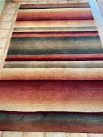 Full view of the ombré area rug displaying horizontal stripes blending reds, rusts, greens, and beige.