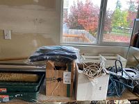 Photo showing boxes containing extension cords, wires, and Makita bag piled with other painting supplies.