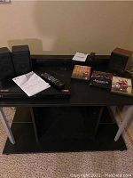 Photo of TV stand with LG Blu-ray player, KLH speakers, TLC sound bar, DVDs, remote controls and manuals arranged on top.