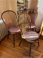Three wooden Windsor chairs arranged in room next to radiator and bookshelf