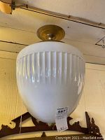 Full view of ceiling light fixture showing white ribbed glass globe and brass ceiling mount.
