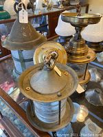 Photo showing two brass and glass nautical style ceiling lanterns with circular glass enclosures and brass mounting bases with patina and wear.