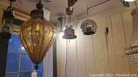 Group shot of three hanging pendants: amber crackled glass, clear glass brass lantern, and chrome sphere
