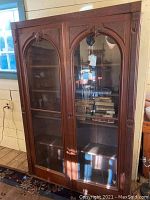 Front view of two-door glass-front bookcase showing four shelves and carved arch details.