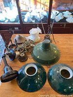 Overview of 3 green enameled metal shades, black gooseneck arm, brass parts and twisted rods on wooden table