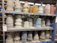 Shelf displaying multiple rows of glass lamp shades varying in size, shape, and color. Shades include frosted and textured designs predominantly in white, blue, and pink shades.