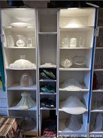 Shelves displaying multiple glass light shades of varying sizes and styles including frosted and clear glass.