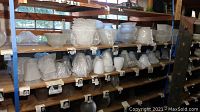 Shelf display showing dozens of mostly white glass lamp shades in various fluted, ribbed and ruffled designs
