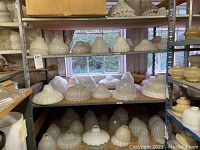 Three-shelf view of milk glass shades on metal shelving.