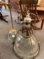 View of two vintage Holophane light fixtures, one with solid brass fixture and the other heavily rusted metal fixture, both with signed ribbed glass shades.