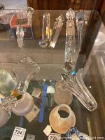 Assorted clear faceted lamp crystals of various shapes and sizes displayed on a glass shelf, including teardrop and geometric shapes.