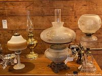 Group view of six electrified antique oil lamps on wooden table against wood wall