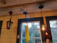 Overview of three hanging light fixtures: antique-style lantern with stained glass, yellow cylindrical pendant, and modern black wire cage pendant with exposed bulb.
