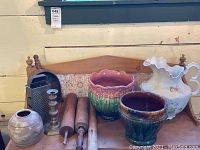 Wide view showing all pottery, wooden rolling pins, metal candlesticks, ceramic pitcher, and metal box grater arranged on wooden surface.
