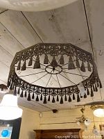 Wide shot of large silver plated ceiling fixture hanging from ceiling, showing shape, size, and decorative details with tassels.