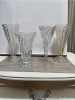 Front view of all four vintage crystal vases arranged in a row on a white surface with a gray mat.