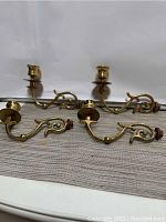 Four solid brass candleholders laid out on a surface showing the curved arms, mounting hardware, and candle cups.