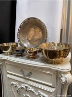 Five silver plate bowls arranged from smallest to largest on a white dresser, showing tarnish and vintage wear.
