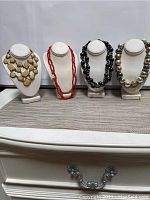 Four assorted costume jewelry necklaces on white necklace displays, shown in one photo to illustrate the complete lot.