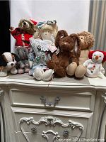 Group photo showing assorted toys including handmade doll, brown bunny, plush dog, grey elephant, Cabbage Patch doll, Ty snowman, and Santa in background