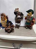Five character figures displayed against white background on woven mat: Beauty and the Beast Beast on the left, a jester figure sitting in front, a Santas-clad man figure in center, and a fox character on the right holding grapes and a sword.