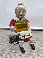 Front view of Grandma Christmas ceramic figurine holding yellow box with green bow, showing detached feet and black cat beside figure.