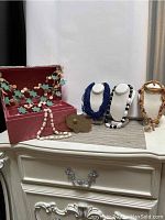 Photo of red patterned jewelry box and several pieces of costume jewelry including necklaces and bracelets on a dresser.