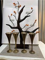 Full front view of metal tree-shaped candelabra with glass candle holders and four hammered brass footed goblets arranged in front.