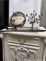 Photo showing all five metal items arranged on a surface, including pig decoration, napkin holder, fork, black tool, and candleholder.