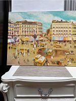 Full view of signed oil painting depicting a busy city street scene with buildings, pedestrians, and horse-drawn carriages.