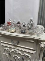 Photo showing multiple clear transparent Christmas ball ornaments on a white vintage style table. Some ornaments are empty, others contain small decorative items like silver beads, pine cones, and ribbons inside.