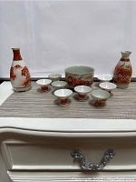 Full set of vintage Kutani Japanese saki items including 2 mini jugs, 1 bowl, 8 cups arranged on a mat.