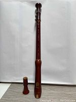 Full view of the upright woodwind instrument and separate accessory piece on a plain background showing its full length.