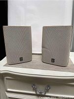 Two beige Yamaha speakers side by side, one has a dent in the front grille.