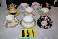 Photo of all ten vintage tea cups with their matching saucers arranged on a table, showing various floral and decorative designs distinct to each manufacturer.