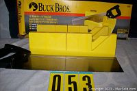 Photo showing the yellow plastic 12-inch miter box alongside the 14-inch backsaw with black handle, both in front of the original Buck Bros. box.