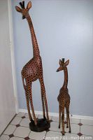 Photo showing both large and small wood carved giraffes standing next to each other against a wall.