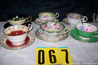 Overview of all 6 tea cups and saucers arranged in two rows showing varied designs and colors against a dark backdrop