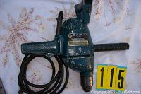 Blue Black & Decker heavy duty drill on a white surface with some pattern, visible wear and chipping on paint, cord coiled and taped, side handle present.