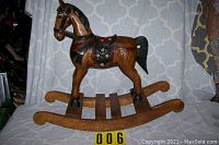 Full side view of the carved wooden rocking horse showing the detailed saddle, mane, tail, and wooden rocker base.