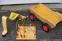 Photo showing the Rifton wagon wooden base with red wheels, KinderWorks bead wire maze with multiple colored beads on twisted metal wire, and Svan of Sweden wooden scooter curved frame with wheels, all arranged on asphalt.