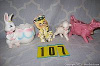 Photo showing four ceramic figurines: Easter Bunny with egg planter, yellow cat with kitten figurine, naturalistic sheep figurine, and pink cow creamer.