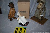 Three decorative figurines: At Home bakery chef in white coat and hat in front of box, carved wood toga man, paper mache woman on wooden base.