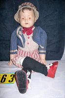 Full length view of the vintage doll sitting on a white surface, showing the outfit, face, and red shoes