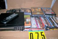 Box containing Curtis DVD player with remote and over 95 DVDs stacked and arranged inside, showing titles and condition of cases.
