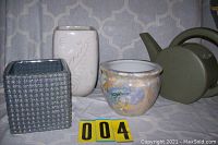 Overview photo of four ceramic items including the gray square pot, beige engraved vase, multicolor round floral pot, and olive green watering pot.